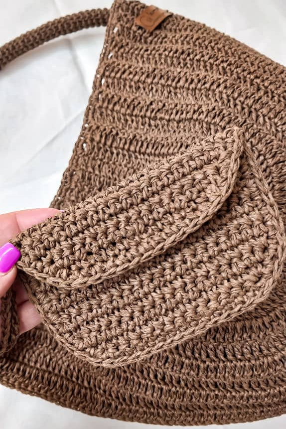 Brown crochet bag held by a hand on a white background