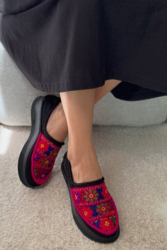 Colorful embroidered slippers worn with a black skirt on a neutral background