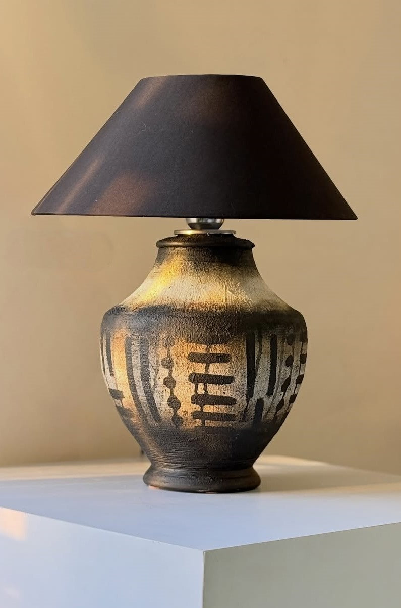 Ceramic table lamp with black shade on a white surface against a beige wall
