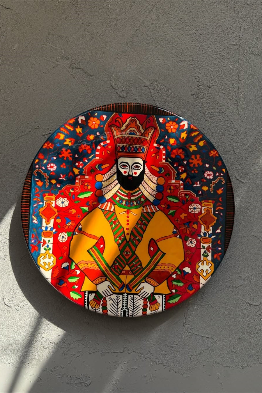 Decorative plate with a colorful design of a seated figure on a gray wall.