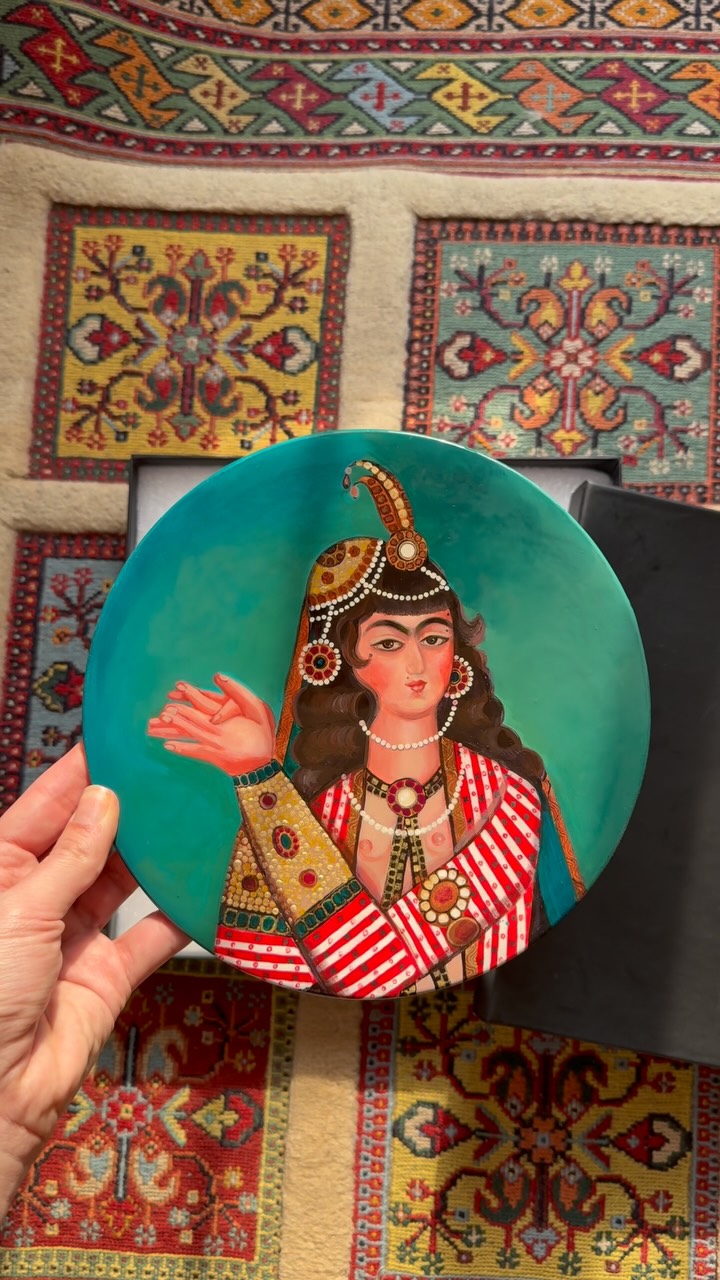 Decorative plate with a traditional design held in front of colorful patterned rugs.