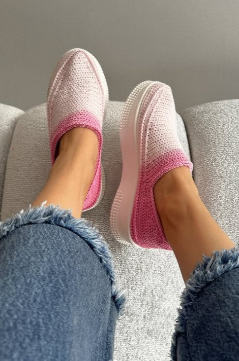 Pink slip-on shoes worn with blue jeans on a neutral background