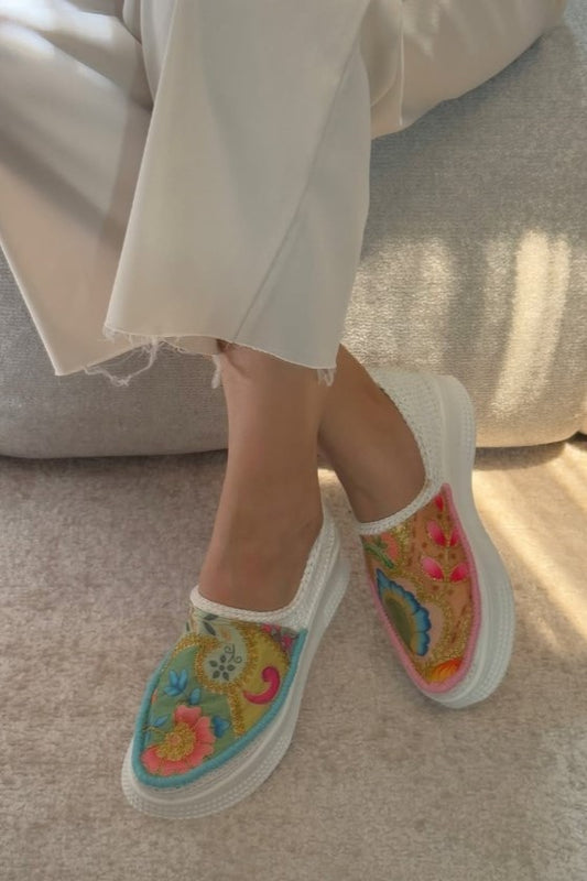 Colorful embroidered slip-on shoes worn with light-colored pants on a neutral background