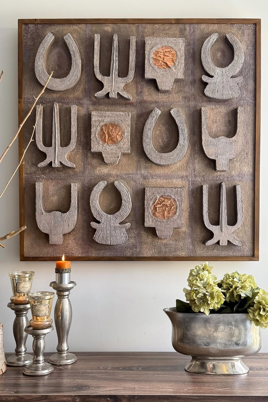 Decorative wall art with geometric shapes on a wooden frame above a wooden console table with decorative items.