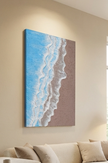 Canvas print of a beach scene with blue water and brown sand hanging on a beige wall above a sofa.