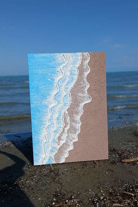 Artistic depiction of a beach scene on a rectangular card with blue water and brown sand, placed on a beach.