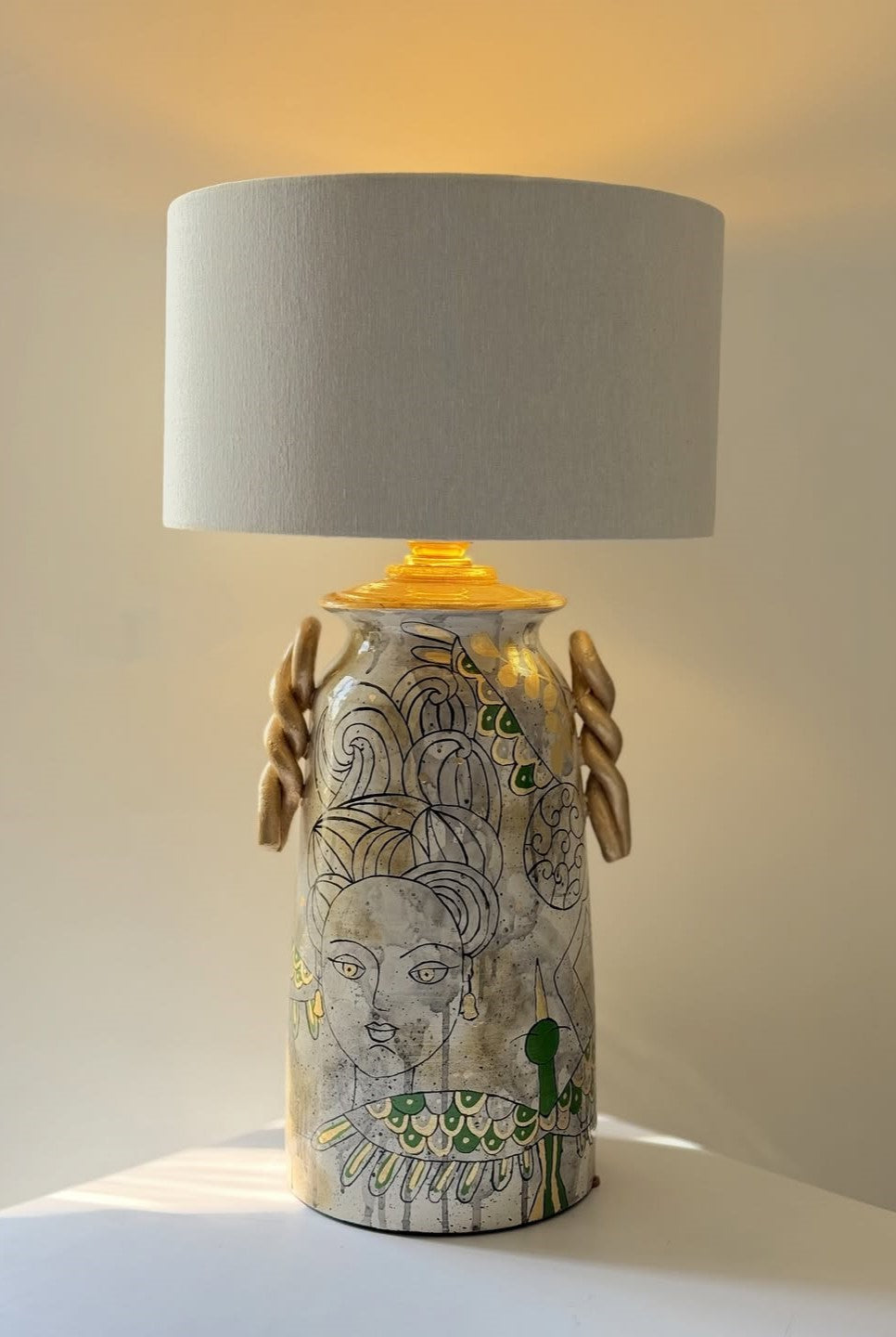 Decorative lamp with a gray shade and artistic base on a white surface.