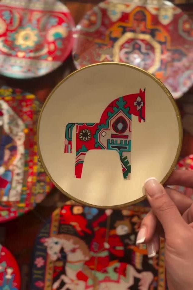 Decorative plate with a colorful horse design held by a hand against a patterned background.
