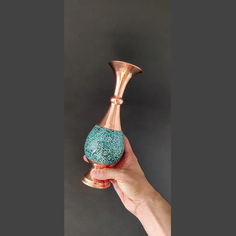 Hand holding a decorative vase with turquoise base and copper top against a dark background