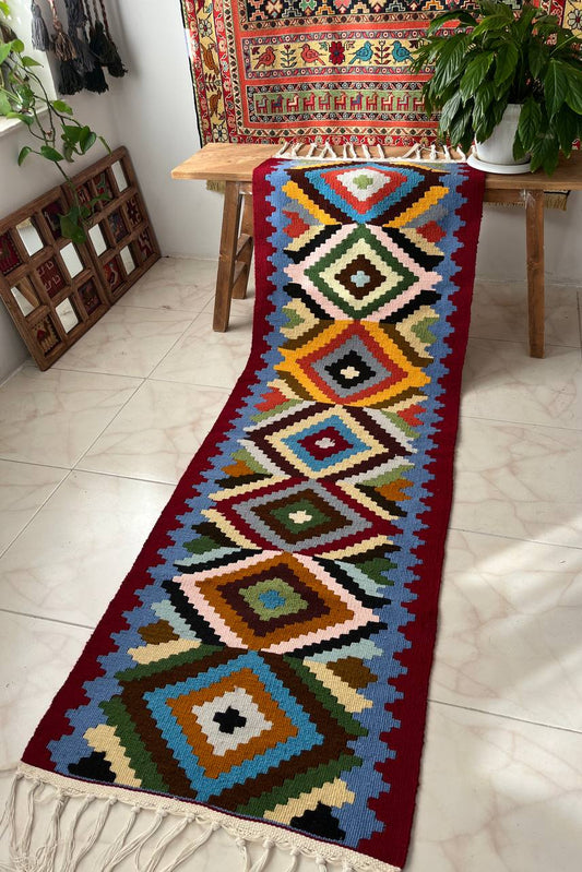 Colorful geometric patterned rug on a tiled floor with a wooden bench and plants in the background.